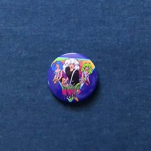 Peut inclure: Un bouton rond violet avec une illustration de dessin animé de trois femmes aux cheveux colorés. La figure centrale a les cheveux blancs et une tenue noire. Le bouton a une esthétique rétro des années 80.