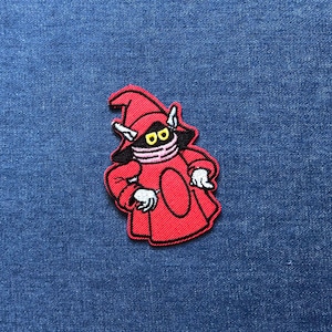 May include: Embroidered patch featuring a red cartoon character with a black face, yellow eyes, and a red hat. The patch has white gloves and is outlined in black. The patch is on a blue denim background.