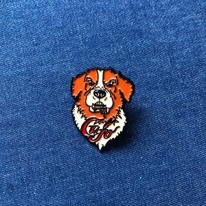 May include: A pin featuring a stylized dog's head with orange, white, and black details. The dog has an angry expression and the word "Cujo" in red script. The pin is set against a blue denim background.