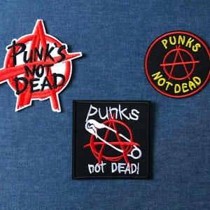May include: Three embroidered patches with the slogan "Punks Not Dead". One is a red and white design, another a black circle with yellow text, and the third a black square with a red and white design.