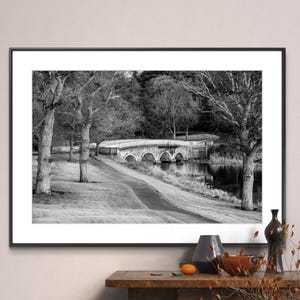 May include: A black and white photograph of a stone bridge over a river. The bridge has five arches and is surrounded by trees. The photo is framed in a black frame.