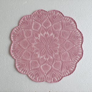 Könnte beinhalten: Eine rosa gehäkelte Tischdecke mit einem zarten Blumenmuster.