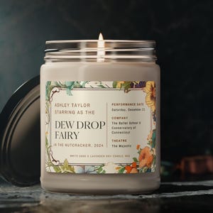 May include: A white sage and lavender soy candle with a floral design label. The label reads "Ashley Taylor starring as the Dew Drop Fairy in the Nutcracker, 2024".
