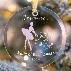 May include: A clear glass Christmas ornament with a ballerina silhouette and the text "Jasmine Waltz of the Flowers 2024".