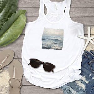 May include: White tank top with a square ocean painting, sunglasses, denim shorts, and flip-flops. The image includes a starfish and large green leaves, creating a beachy, summery vibe. The tank top features a square painting of the ocean.