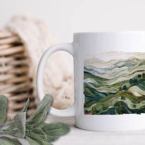 May include: White ceramic mug with a green and brown landscape design. The design features rolling hills and trees.