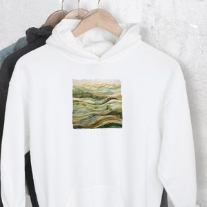 May include: White hooded sweatshirt with a green, brown, and beige landscape design on the front.