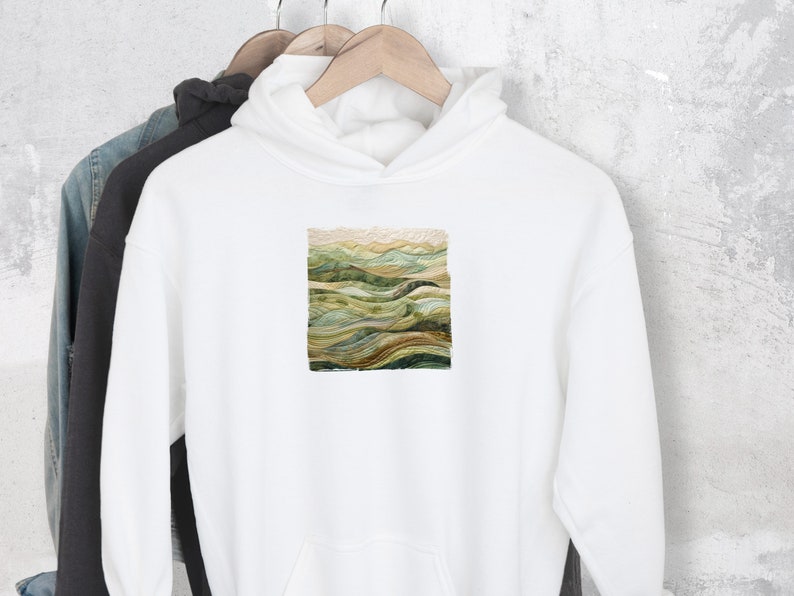 May include: White hooded sweatshirt with a green, brown, and beige landscape design on the front.