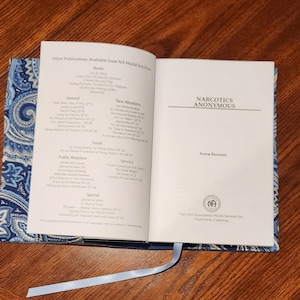 Puede incluir: Un libro cerrado con una cubierta de patrón azul y blanco. El libro se titula "Narcotics Anonymous" y es la sexta edición. El libro es publicado por Narcotics Anonymous World Services, Inc. en Chatsworth, California.
