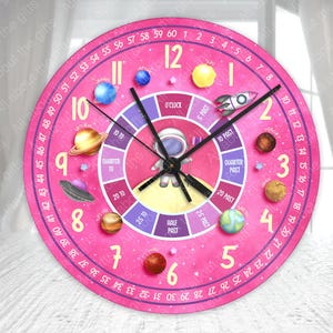 May include: Pink analog clock with a space theme. The clock face features a cartoon astronaut, planets, and stars. The numbers are in a circle around the clock face, and the clock hands are black. The clock face also includes a smaller circle with the words "O'Clock", "5 Past", "10 Past", "Quarter Past", "20 Past", "25 Past", "Half Past", and "Quarter To".