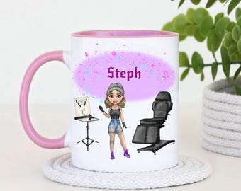 Könnte beinhalten: Eine weiße Keramiktasse mit rosafarbenem Rand und Henkel. Die Tasse zeigt eine Comic-Illustration eines Tätowierers mit einer Tätowiermaschine und einem Kunden in einem Tätowierstuhl. Die Tasse trägt den Namen "Steph" in lila.