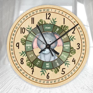 Puede incluir: Un reloj de pared redondo de madera con una ilustración de un elefante gris. La esfera del reloj tiene manecillas negras, hojas verdes y números. El reloj mide aproximadamente 30 cm de diámetro.