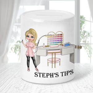 Op de afbeelding: Witte keramische spaarpot met een nagelsalon thema. De spaarpot heeft een illustratie van een blonde vrouw in een roze uniform, nagellakflesjes en een nagelstudio. De tekst "STEPH'S TIPS" staat op de voorkant.