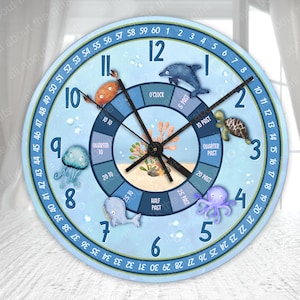 Op de afbeelding: Een blauwe en witte ronde klok met een zeethema. De wijzerplaat van de klok heeft de cijfers 1 tot en met 12, evenals de woorden "O'Clock", "5 Past", "10 Past", "Quarter Past", "20 Past", "25 Past", "Half Past", "Quarter To", "20 To", "10 To" en "5 To". De klok is versierd met afbeeldingen van een kwal, een dolfijn, een zeeschildpad, een octopus en een zeepaardje.