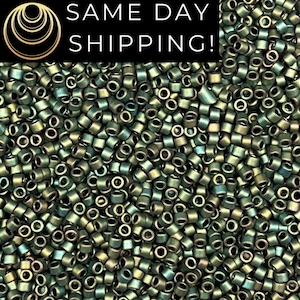 May include: A large collection of small, cylindrical glass beads with a metallic, iridescent finish. The beads display a dark, muted green color with subtle hints of bronze and gold reflections, creating a uniform, textured appearance.