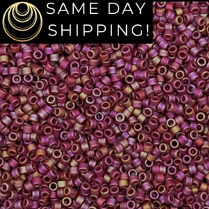 May include: A close-up image of a large quantity of small, round, iridescent beads. The beads are a deep burgundy color with a subtle gold shimmer.