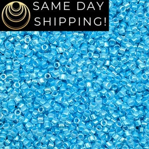 May include: A large collection of small, cylindrical, light blue glass seed beads with a translucent finish. The top of the image features a black rectangular banner with a gold circular logo and the white text SAME DAY SHIPPING!