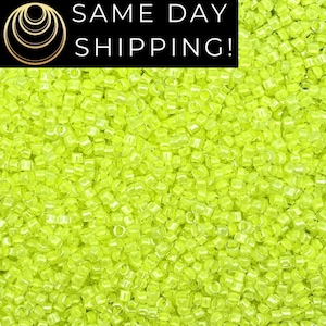 May include: A close-up image of a large quantity of small, bright yellow, glass seed beads. The beads are uniform in size and shape, and they have a slightly iridescent finish.