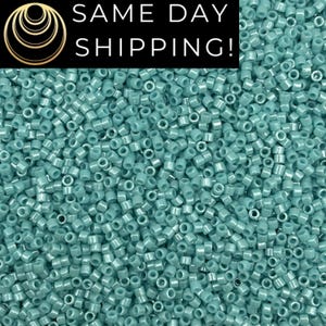 May include: A close-up shot of a large pile of small, cylindrical, turquoise-colored seed beads. The beads are densely packed, filling the frame. The image includes the text "SAME DAY SHIPPING!" in a black box.