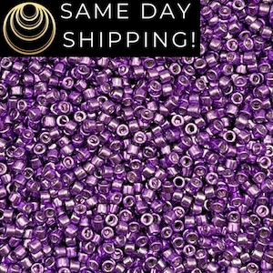 May include: A close-up image of a large quantity of small, round, metallic purple beads. The beads are all the same size and shape, and they are arranged in a random pattern.