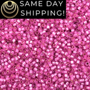 May include: A close-up image of a large quantity of small, pink, round seed beads with a metallic sheen. The beads are arranged in a random pattern, creating a textured surface.