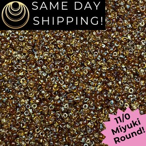 May include: A large collection of small, translucent amber-colored glass beads. The image includes text that reads SAME DAY SHIPPING! and a pink starburst graphic with the text 11/0 Miyuki Round! The beads are round and uniform in size.