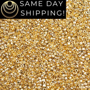 May include: A close-up image of a large quantity of small, gold-colored seed beads. The beads are round and have a metallic finish.