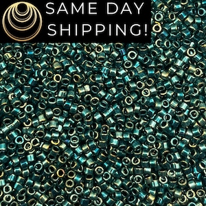May include: A close-up image of a large quantity of teal green seed beads. The beads are small and round with a metallic sheen.