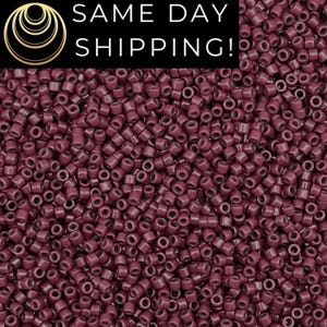May include: A close-up image of a large quantity of small, round, dark red beads. The beads are all the same size and shape, and they are arranged in a random pattern.