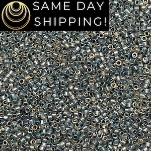 May include: A close-up view of a large quantity of small, silver-colored seed beads. The beads are cylindrical with a hole running through the center. The image also contains the text "SAME DAY SHIPPING!"