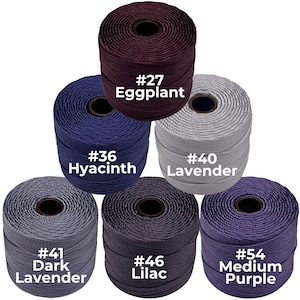 May include: A collection of six spools of cord in various shades of purple, blue, and gray. Each spool is labeled with a color name and number, including "Eggplant," "Hyacinth," "Lavender," and "Lilac." The cords are tightly wound.