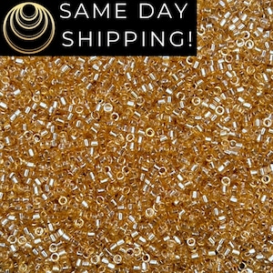 May include: Close-up of a pile of small, golden-colored seed beads. The beads are cylindrical with a hole running through the center. The image also contains the text "SAME DAY SHIPPING!"