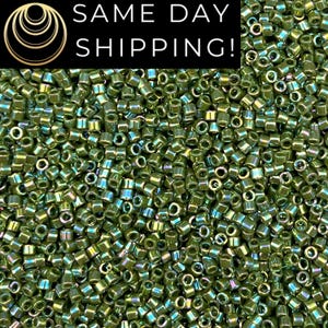 May include: Close-up of a pile of olive green seed beads. The beads have a cylindrical shape with a small hole running through the center. The beads have an iridescent sheen, reflecting multiple colors. The text "SAME DAY SHIPPING!" is at the top.