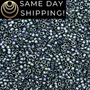 May include: A large collection of small, cylindrical, metallic-finish beads in shades of dark grey, purple, and green. The beads have a uniform shape and a reflective surface. A black banner at the top displays the text SAME DAY SHIPPING!