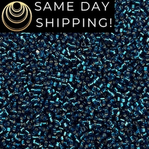 May include: A close-up image of a large quantity of small, teal blue seed beads. The beads are metallic and have a shiny finish.