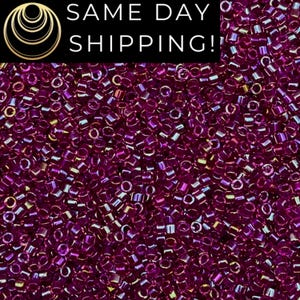 May include: A close-up image of a large quantity of small, round, iridescent purple beads. The beads have a metallic sheen and are arranged in a random pattern.