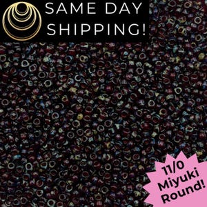 May include: A collection of 11/0 Miyuki round beads in a deep, dark burgundy color with iridescent, multi-colored highlights. The beads are small, uniform, and spherical with a central hole, featuring a glossy finish and scattered light reflections.