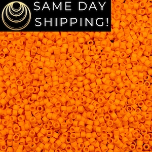 May include: A large collection of small, cylindrical, matte orange beads arranged in a dense, uniform layer. Each bead features a central hole, creating a consistent, repetitive texture across the entire surface of the image.