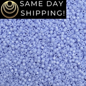 May include: A close-up view of a large quantity of small, light purple seed beads. The beads are round and have a smooth, glossy finish.