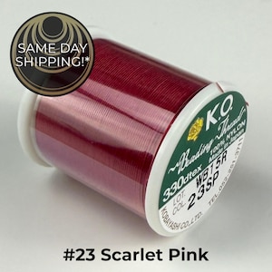 May include: A spool of K.O. Beading Thread in scarlet pink color. The label on the white plastic spool indicates 100% nylon, 330dtex, and the color code 23SP. The text #23 Scarlet Pink is printed below the spool on a plain background.