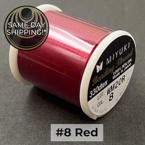 May include: A spool of deep red Miyuki beading thread made of 100% nylon. The white label on the side displays the text Miyuki Beading Thread, 330dtex, 100% Nylon, Made in Japan, Lot WM20R, and Col. 8. The spool has white plastic ends.