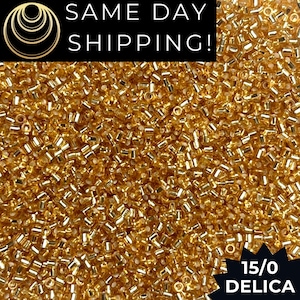 May include: A close-up shot of a pile of small, golden-colored Delica beads. The beads are cylindrical and have a metallic sheen. The text "SAME DAY SHIPPING!" is at the top, and "15/0 DELICA" is at the bottom.