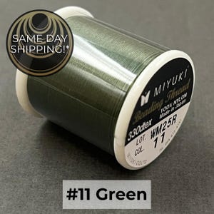 May include: A spool of olive green Miyuki beading thread made of 100% nylon. The label displays the text Miyuki Beading Thread, 330dtex, 100% Nylon, Made in Japan, Lot WM25R, Col 11, and the text #11 Green is visible below the spool.