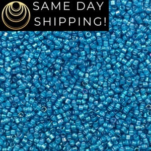 May include: A close-up shot of a pile of small, cylindrical, turquoise-colored glass beads. The beads are scattered, creating a textured surface. The image includes the text "SAME DAY SHIPPING!" in white letters on a black background.