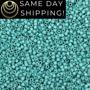 May include: A close-up image of a large quantity of small, turquoise blue, round seed beads. The beads are all the same size and shape, and they are arranged in a random pattern.