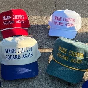 Puede incluir: Ocho gorras de béisbol con el texto "Make Chevys Square Again" en bordado blanco sobre gorras de varios colores. Las gorras están dispuestas sobre una superficie de hormigón gris.