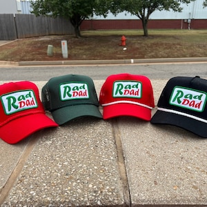 Peut inclure: Quatre casquettes de camionneur avec un patch "Rad Dad" vert et blanc sur le devant. Les casquettes sont rouge, verte, noire et blanche.