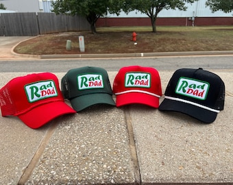 May include: Four trucker hats with a green and white "Rad Dad" patch on the front. The hats are red, green, black, and white.