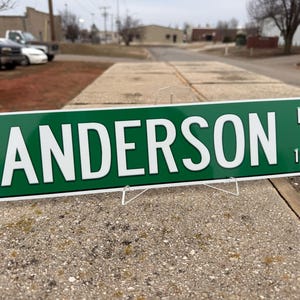 以下が含まれることがあります： 緑色の街路標識に白い文字で「Anderson LN 1956」と書いてあります。