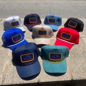 May include: A collection of ten trucker hats with a variety of colors and designs. Each hat features a patch with the text "GMC TRUCKS" in a blue, red, and yellow color scheme.